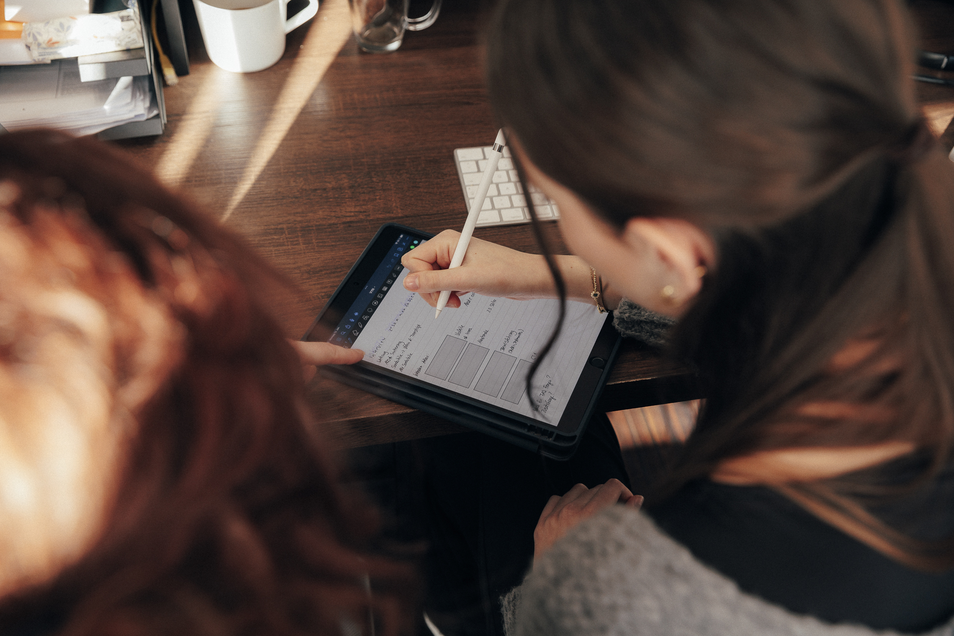 Zwei Personen sitzen vor einem Tablet und schreiben etwas darauf