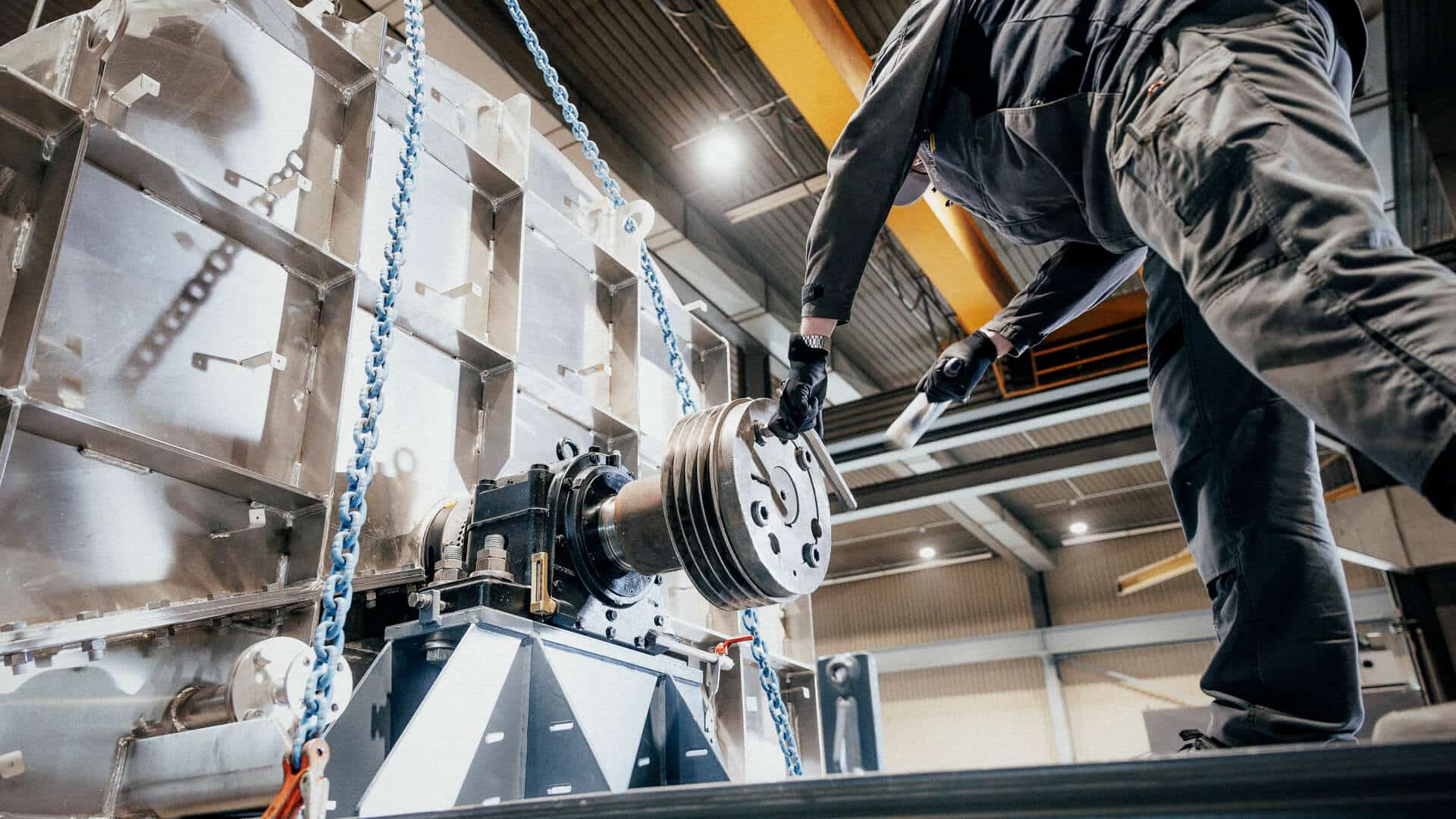 Mann arbeitet in Halle an einer Maschine und haut mit einem Hammer auf einen Imbussschlüssel an einem Zylinder