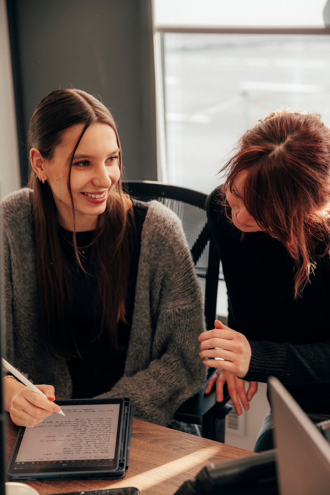 Zwei Personen tauschen sich lächelnd vor einem Tablet aus.