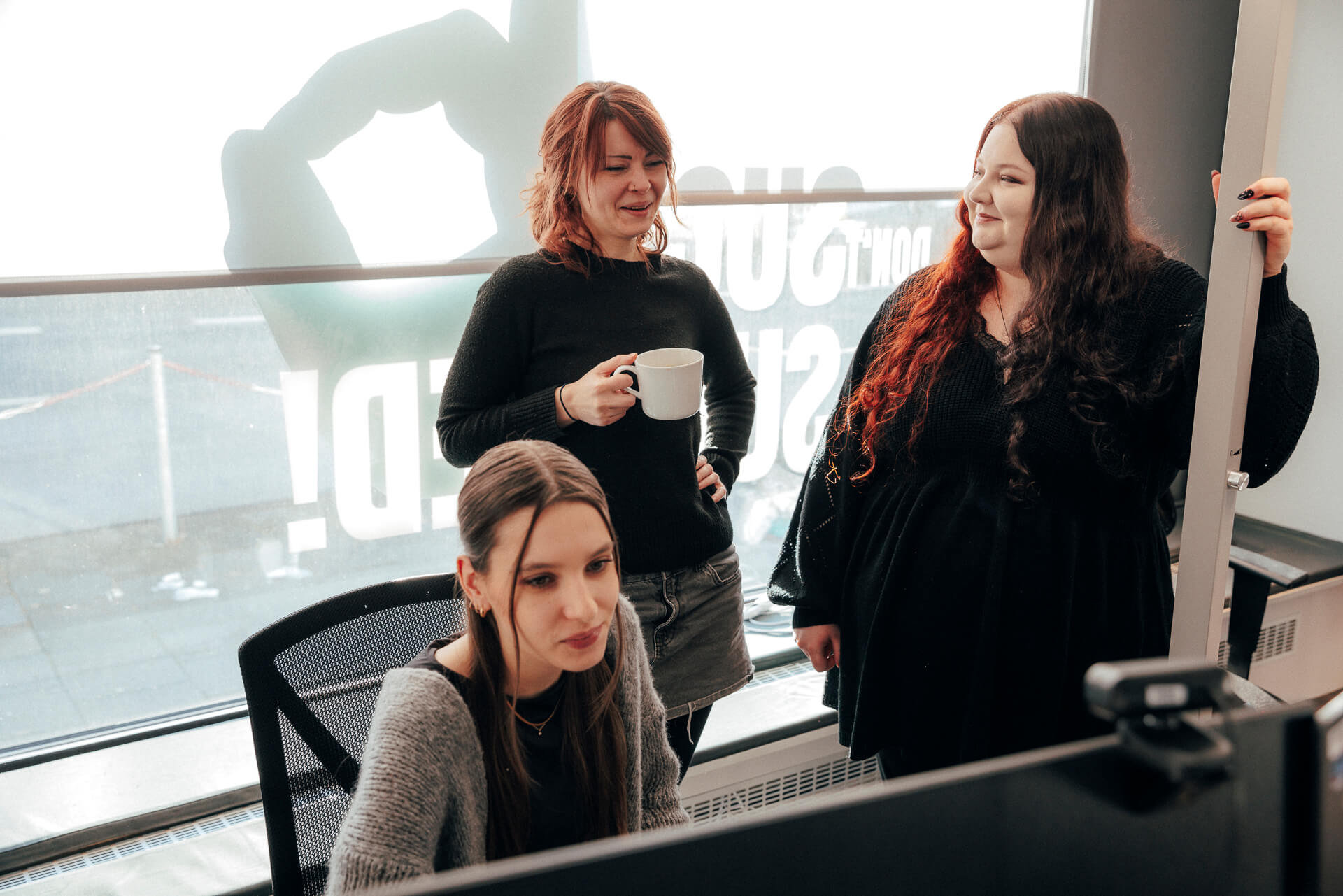 Drei Personen sitzen und stehen lächelnd vor einem Bildschirm