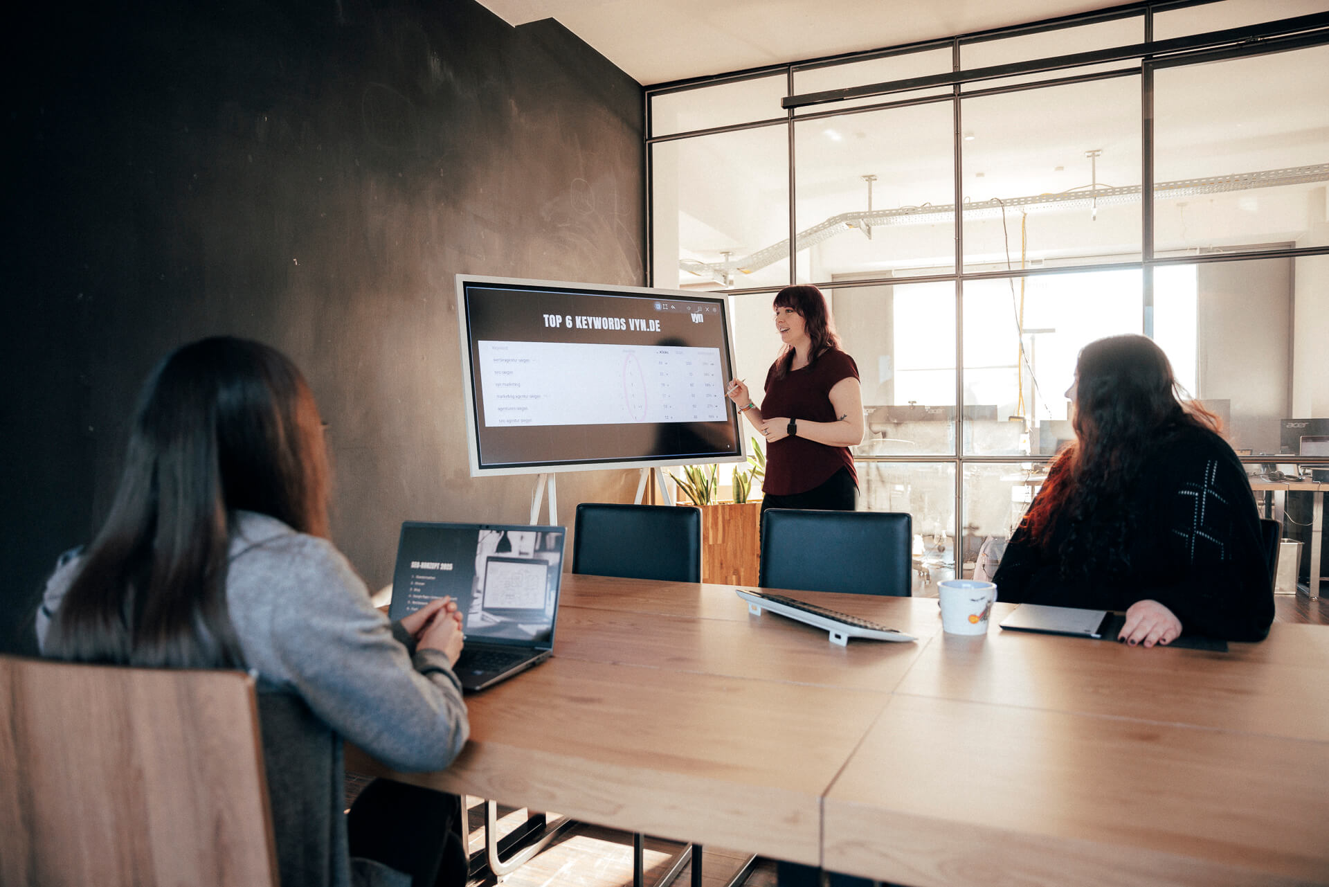 Zwei Personen sitzen an einem Tisch, während eine andere eine Schulung abhält