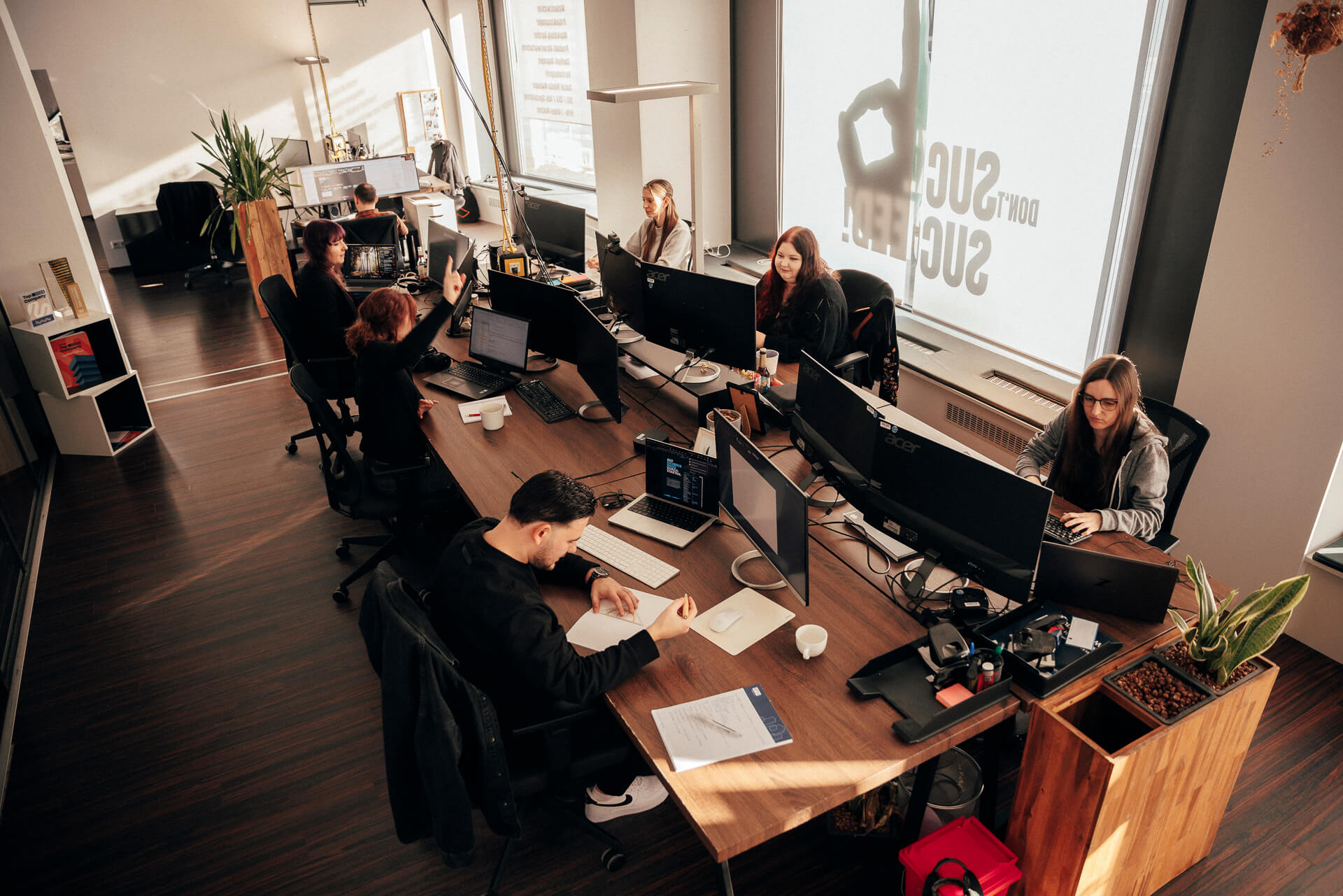 Sieben Personen sitzen am Computer an ihrem Arbeitsplatz